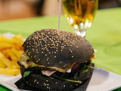 Hamburger con pane nero, patatine e birra su tavolo verde.