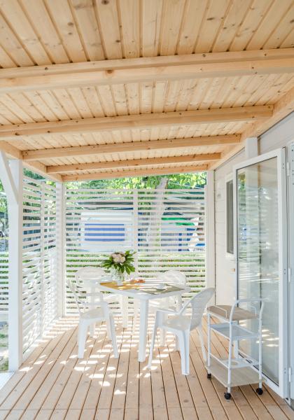 Wooden covered terrace with white table and chairs, decorated with flowers.