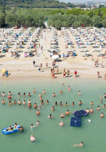 Spiaggia affollata con persone che nuotano e prendono il sole sotto ombrelloni.