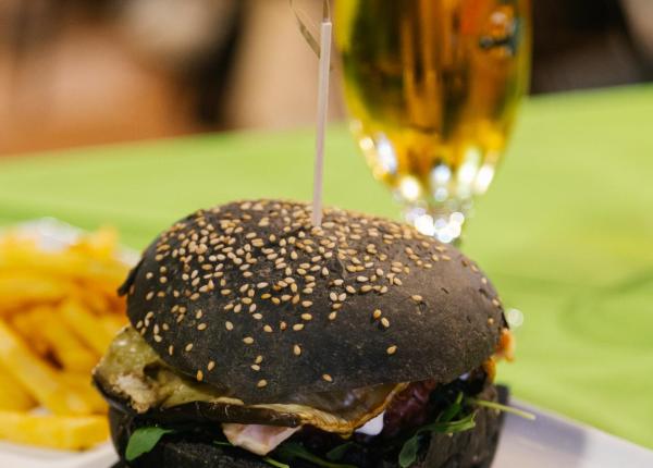 Hamburger con pane nero, patatine e birra su tavolo verde.